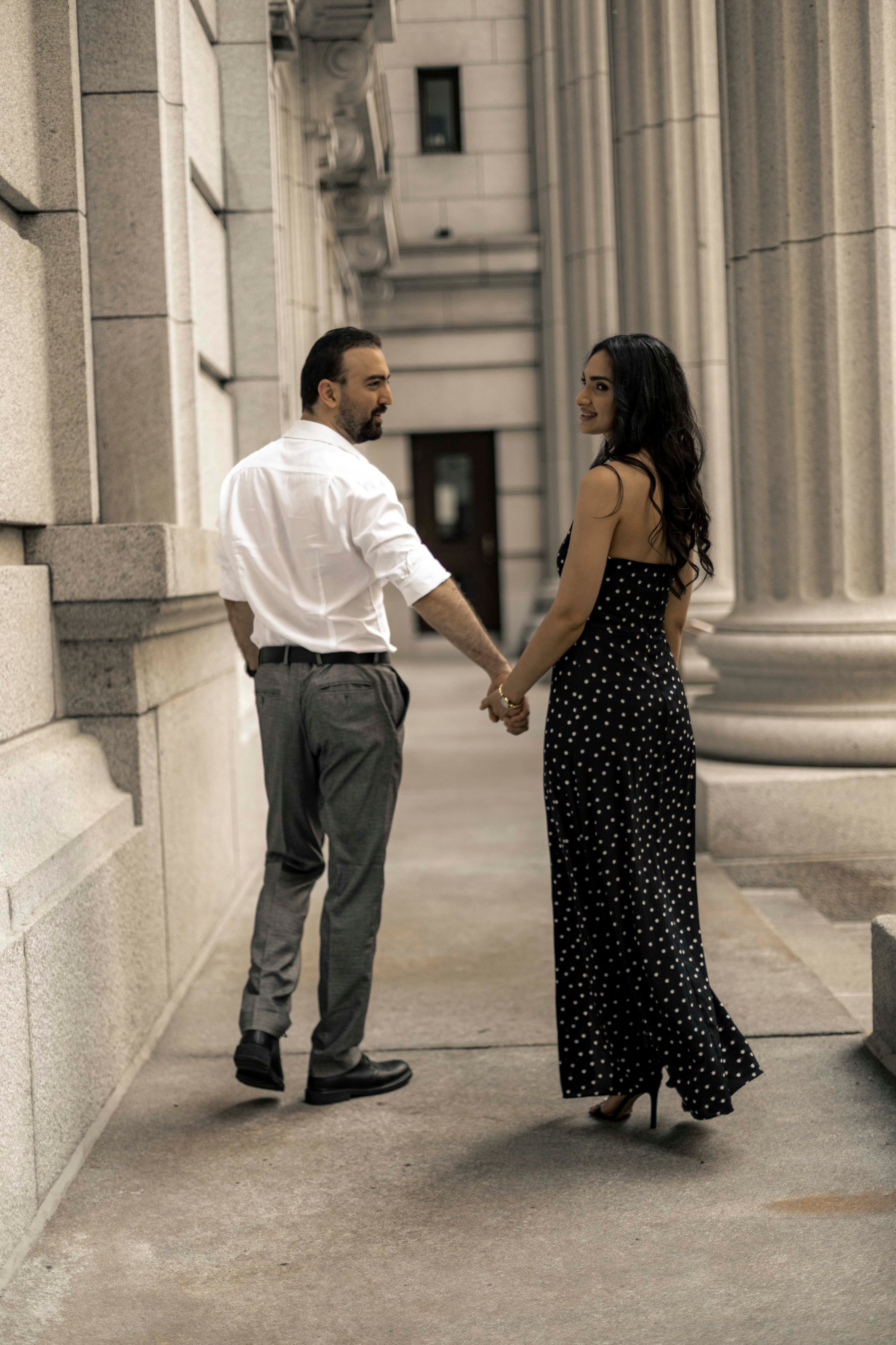 A couple walking hand in hand past stone columns