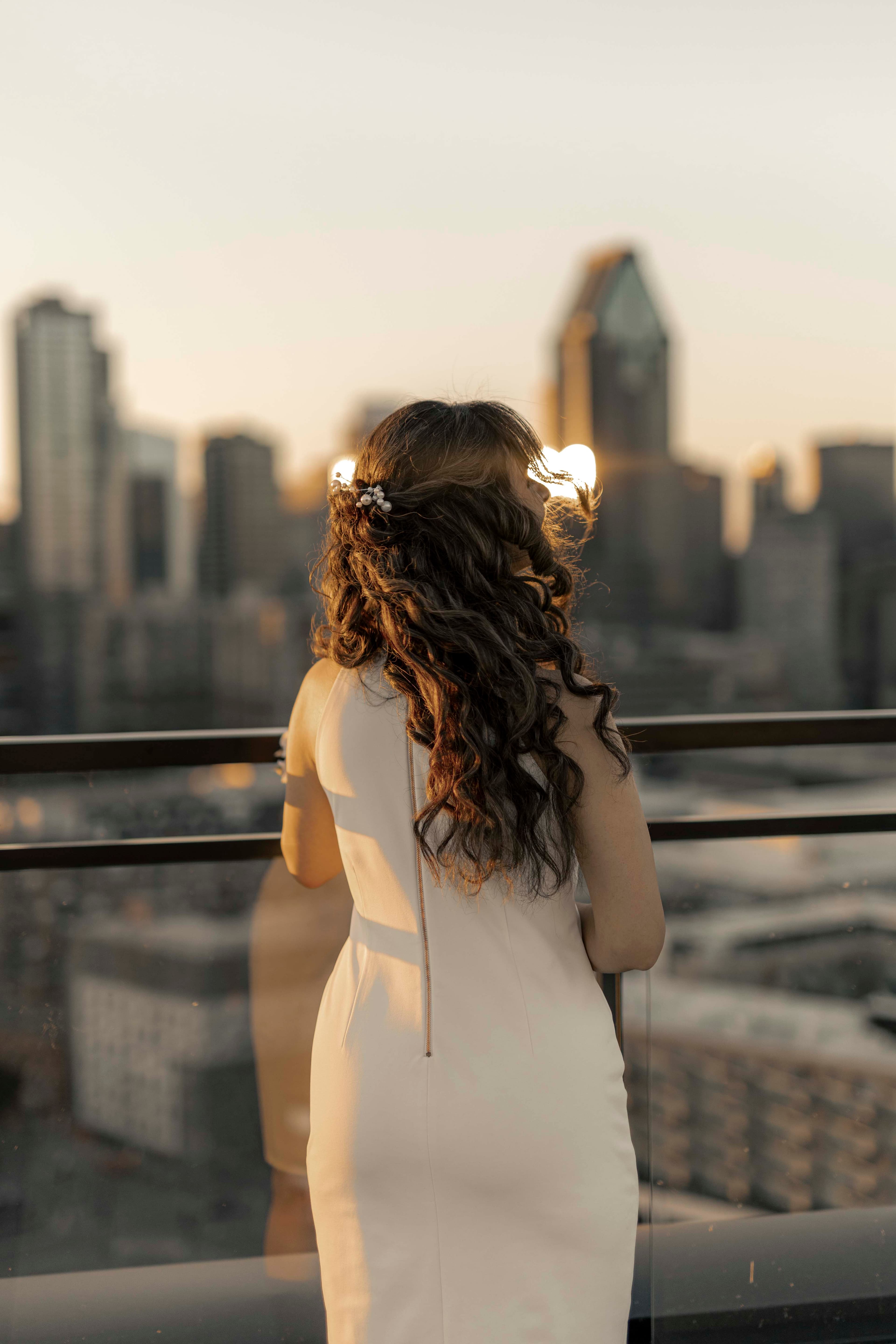 A bride on a rooftop at sunset, the city skyline behind her
